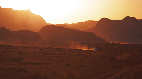 A vehicle drives through the red desert kicking up dust at sunset in Wadi Rum
