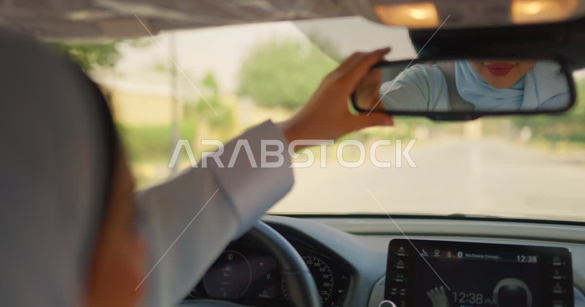 Adjusting the car’s rearview mirror, reflecting the image of a veiled