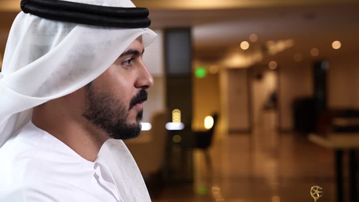 Drinking a delicious hot drink, enjoying a favorite beverage, a close-up shot from the side of a young Emirati Gulf Arab man wearing a kandura and ghutra drinking a cup of coffee, enjoying drinks from cafes and ready-made restaurants