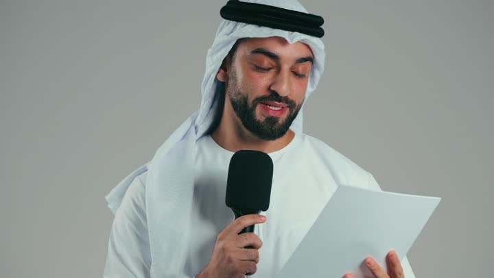 تبادل الحوار والنقاش والتواصل الفعال، القاء الخطابات من الورقة بإيماءات الثقة بالنفس، تقديم ورش العمل والدورات التدريبية، فن التحدث والخطابة، بورتريه لشاب عربي خليجي اماراتي يرتدي الكندورة والغترة يقف بثقه يمسك مكبر الصوت، خلفيه رماديه