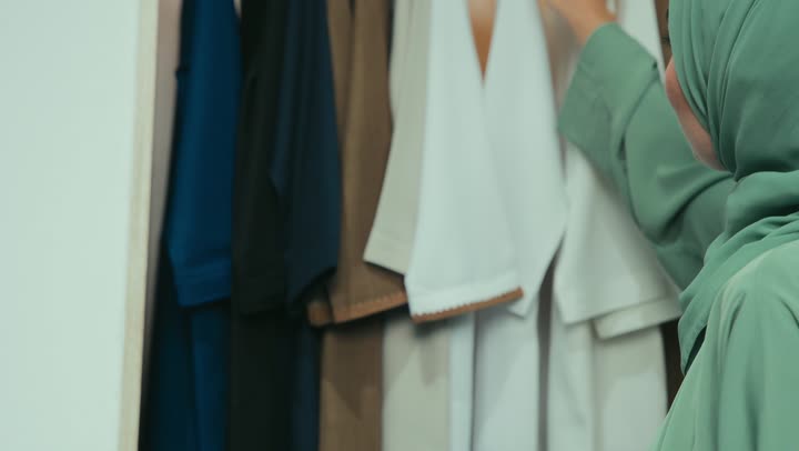 Shopping for women's essentials from the store, taking advantage of offers and discounts, a close-up of an Emirati Gulf Arab woman wearing an elegant abaya choosing clothes and abayas from a modern collection, a Saudi woman enjoying a relaxing shopping experience, and strolling inside a luxury shopping mall.