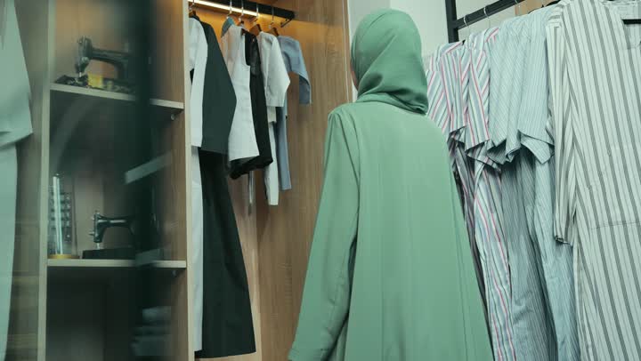 تصوير مقرب لامرأة عربية خليجية إماراتية ترتدي عباءة أنيقة تقوم باختيار ملابس وعبايات من تشكيلة حديثة، سيده سعوديه تقوم بتجربة تسوق ضمن أجواء مريحة ، شراء المستلزمات النسائيه من المتجر ، التجول داخل مول تجاري فاخر.