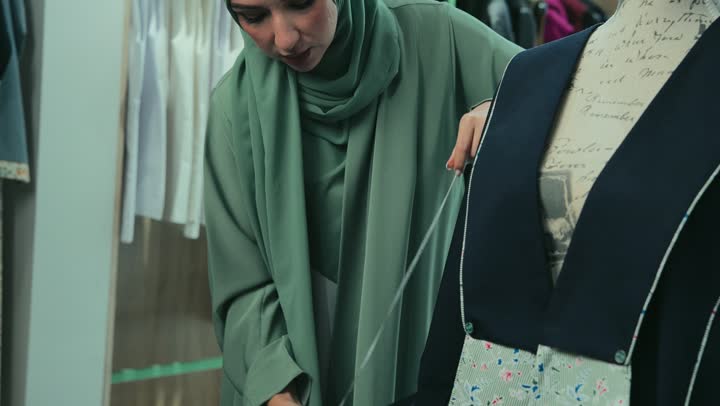 Buying new clothes and accessories, a photo of an Emirati Gulf Arab woman wearing an abaya, taking the abaya size using a measuring tape, the profession of sewing and tailoring modern clothes, a Saudi woman measuring the length of the sleeve, fashion show and new models