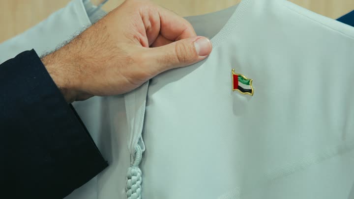 تصوير مقرب لزبون عربي خليجي اماراتي مبتسم يرتدي كندورة كحلي يقوم باختيار ثوب من متجر من متجر المستلزمات الرجاليه ، الاستمتاع بالتسوق في المول التجاري في الامارات العربيه المتحده، إيماءات السعادة و السرور،الاستفادة من العرض و الخصم الموسمي.