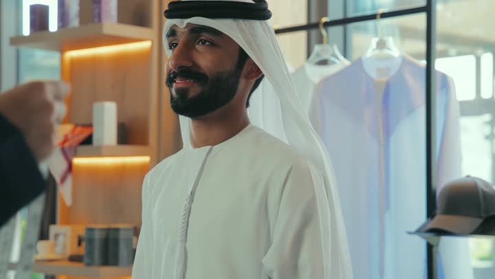 Skill in tailoring youth clothes, men's tailoring and tailoring shop, close-up of a young Emirati Gulf man wearing a navy blue kandura taking measurements of a customer's body using a tape measure, mastery of making clothes, concept of the world of fashion and style, practicing the tailoring profession, handicrafts and crafts.