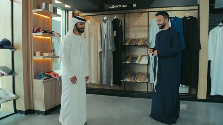 Handicrafts and crafts, practicing the tailoring profession, close-up of a young Emirati Gulf man wearing a navy blue kandura taking measurements of a customer's body using a tape measure, a men's tailoring and tailoring shop, sewing skills and mastery of tailoring youth clothing