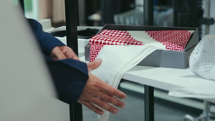 Mastering tailoring clothes, enjoying shopping and buying clothes, a men's tailoring and tailoring shop, a close-up of an Emirati Gulf Arab young man wearing a navy blue kandura working in tailoring, showing the customer the finest types of fabrics for tailoring the thobe