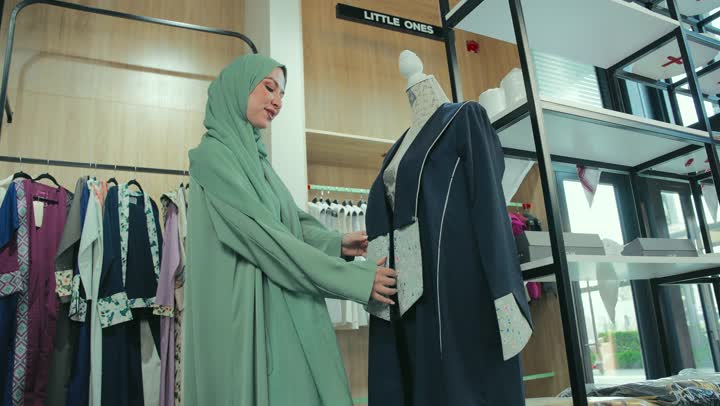 Enjoy shopping in a clothing store, women's clothing with modern designs, a photo of a smiling Emirati Gulf Arab woman wearing an elegant colorful abaya, women's abayas with distinctive modern designs, a Saudi woman buying new clothes, veiled fashion, following fashion and trends