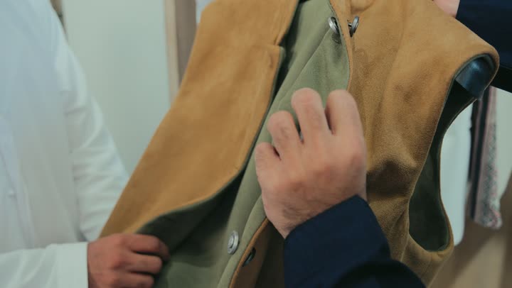 محل خياطة و تفصيل الملابس الرجالي، اختيار أجود أنواع الأقمشة لصنع الثياب، ملابس شتويه دافئه ، متعه التسوق و شراء الملابس، تصوير ليد شاب عربي خليجي اماراتي يرتدي الكندورة الكحلي يعمل في مهنة الخياطة يقوم بعرض جاكيت شتوي للزبون
