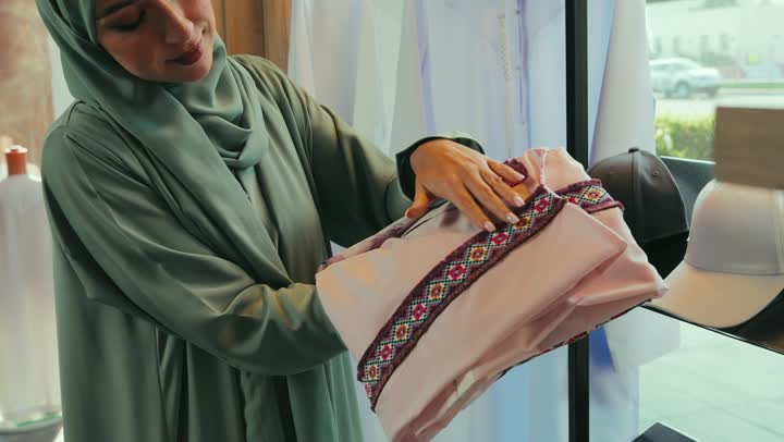 شراء عباءات عصرية حديثه في متجر من السوق في الامارات العربيه المتحده ، تصوير مقرب لامراة عربيه خليجيه اماراتية ترتدي العباءه تقوم بشراء عباءه جديده , مهنة الخياطه وتفصيل الثياب العصريه الحديثه,عرض الأزياء والموديلات الجديده