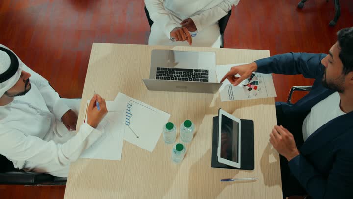 الوحدة والعمل الجماعي لتطوير الأعمال وحل المشكلات، مراجعة التقرير السنوي، استخدام التقنية الحديثة المتطورة، دراسة ومناقشة سير استراتيجية العمل، تصويرمن الاعلى لرجال اعمال يجلسون في المكتب داخل مقر الشركة, الاتفاق على المشروع التجاري، مهنة ووظيفة اماراتية