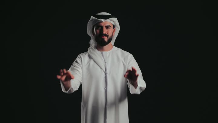 Expressing quality and perfection, cheerfulness, looks of enthusiasm and satisfaction, approval, acceptance and advice, a picture of a smiling young Emirati Arab man wearing the Emirati kandura and ghutra, raising his hands in gestures of quality, excellence and distinction.