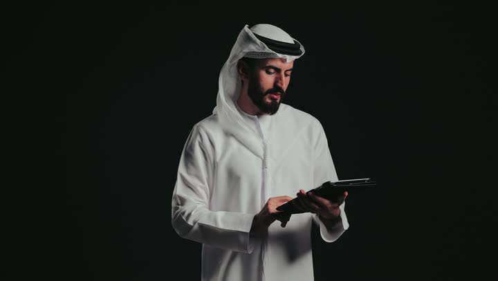 متابعه الخطط والمشاريع ، تدوين وتسجيل الملاحظات والمعلومات على الورق, تنظيم وإدارة الأعمال، تصوير مقرب لشاب عربي خليجي اماراتي يرتدي الكندورة والغترة يقوم بكتابة المهام والأهداف اليومية .