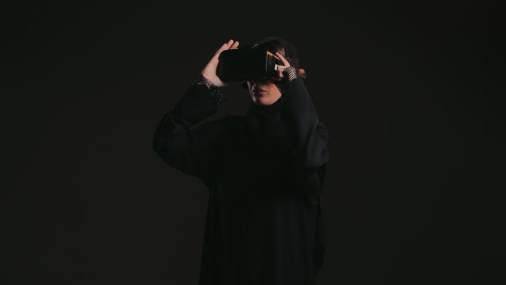 Digital transformation and technological advancement, the use of modern and advanced technologies, gestures of integration and focus in virtual reality, a close-up of an Arab Gulf Emirati woman wearing an abaya and hijab and VR glasses.