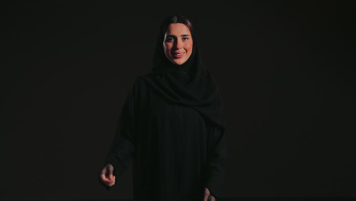 Oral health care and attention, a Hollywood smile using porcelain veneers, a portrait of an Emirati Gulf Arab woman wearing an abaya and hijab pointing her finger at her teeth, teeth beautification and whitening.
