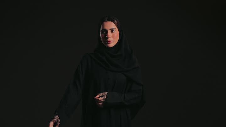 رفع اليد بايماءات التحديد ، إشارات وحركات يدين تدل على هذا المكان (هنا)، سيدة سعودية تقوم بتحديد موقع شيء معين، تصوير لامرأة عربية خليجية إماراتية ترتدي عباءة وحجاب تشير بيديها إلى جهة اليسار .