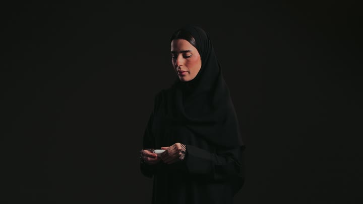Mobile accessories concept, close-up of a Saudi Arabian Gulf man wearing Saudi attire, looking at the camera with a smile and holding a modern Bluetooth headset, mobile devices and technology.