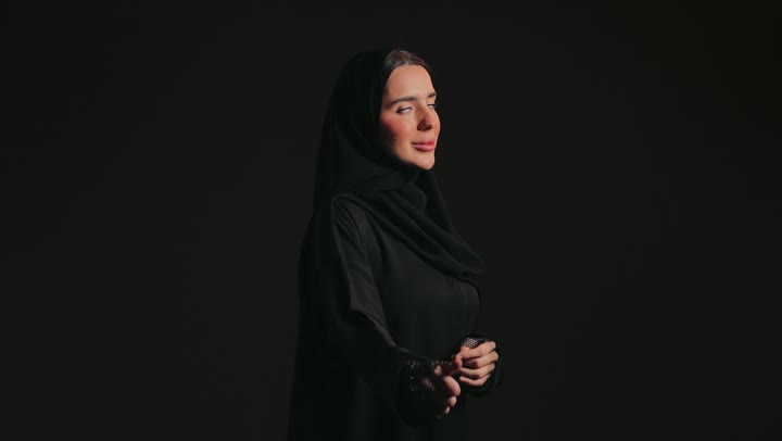 ايماءات الجودة والامتياز ، تعابير الأنوثة والنعومة ، سيدة سعودية مبتسمة تنظر الى الكاميرا وترفع يدها بتعابير الموافقة , الاهتمام بالأناقة والاعتناء بالمظهر الخارجي، تصوير مقرب لإمرأة عربية خليجية إماراتية ترتدي العباءة السوداء  .