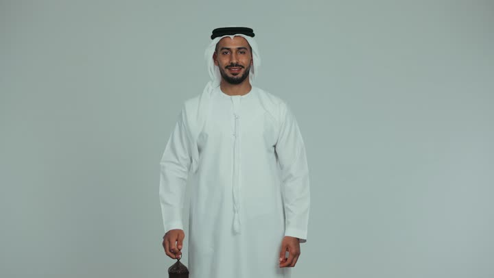 Celebrating religious occasions, preparing for the arrival of the holy month of Ramadan, looking at the camera with gestures of pleasure and happiness, an atmosphere of serenity and spirituality, an Arab Gulf Emirati man wearing a kandura and ghutra holding a metal lantern, white background