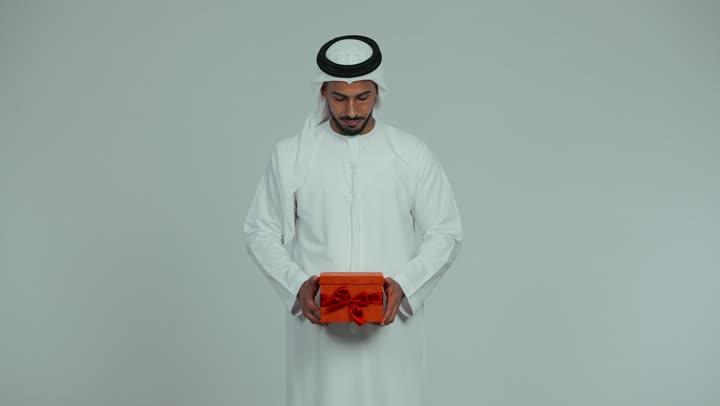 أعياد ومناسبات ومفاجآت سعيدة، رجل عربي خليجي إماراتي يرتدي الكندورة والغترة يقوم بتقديم هدية بإيماءات السعاده والسرور، تقديم الهدايا بين الأهل والأصدقاء، التعبير عن المحبة والألفة، خلفية بيضاء