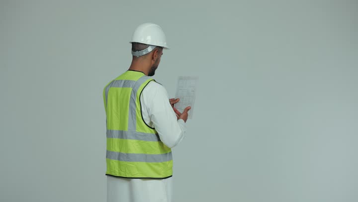 Supervising and auditing work, working in the engineering field, the concept of engineering and architectural construction, a side view of an Emirati Gulf Arab man wearing a kandura, helmet and protective vest, auditing engineering plans and projects, construction by the hands of the sons of the nation, white background.