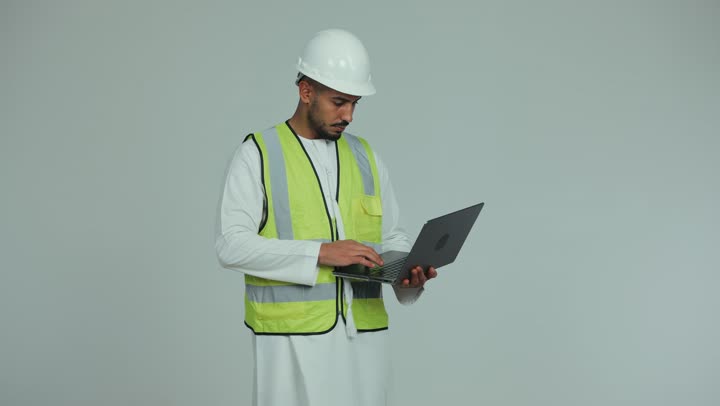 Pointing the index finger at something, managing projects using modern technologies, building the nation with the hands of its sons, an Arab Gulf Emirati man wearing a kandura, helmet and protective vest, following up and checking construction plans using a laptop, working in the engineering sector, white background