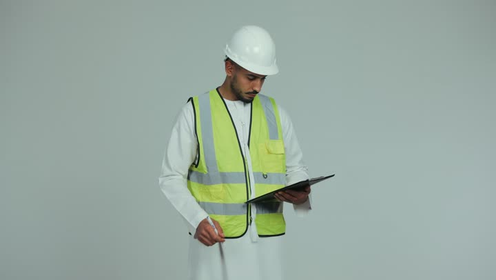 Working in the engineering field, the concept of engineering and architectural construction, supervising and auditing work, an Arab Gulf Emirati man wearing a kandura, helmet and protective vest taking notes on engineering plans and projects, construction by the hands of the sons of the nation, white background.