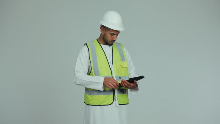 إدارة المشاريع باستخدام التقنيات الحديثة، بناء الوطن بسواعد أبنائه, رجل عربي خليجي اماراتي يرتدي الكندورة والخوذة وسترة الحماية يقوم بمتابعة وتدقيق المخططات الإنشائية باستخدام جهاز التابلت، العمل في القطاع الهندسي، خلفية بيضاء