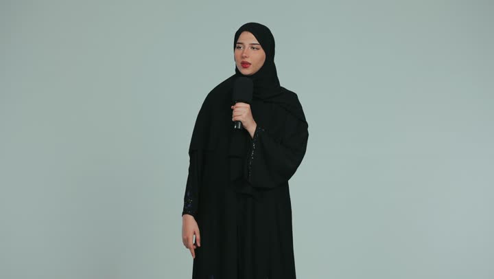 Working in radio and news broadcasting, a young veiled Emirati Gulf Arab woman wearing an abaya holding a loudspeaker, giving lectures and speeches and holding training workshops, women's professions and jobs in the United Arab Emirates, white background