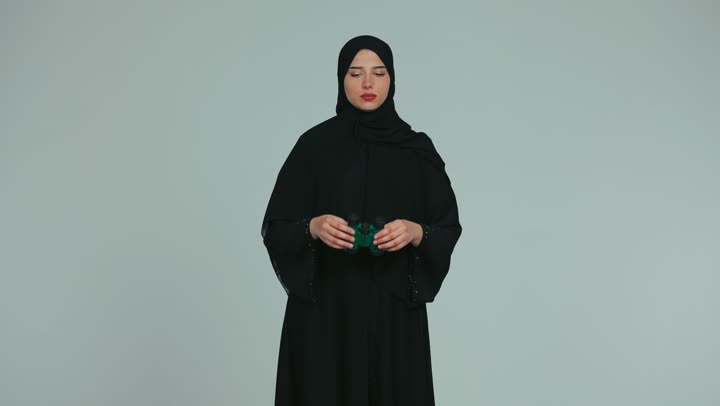 Pointing with index finger at something, observing and watching distant things, future vision and setting goals and ambitions, smiling veiled Emirati Gulf Arab woman wearing an abaya holding binoculars in her hands and looking through them with gestures of pleasure, white background
