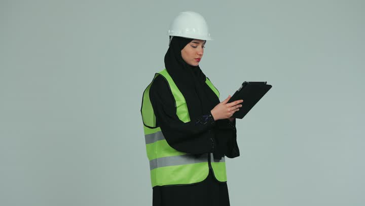 Supervising and auditing work, a veiled female Emirati Gulf Arab engineer wearing a helmet and a protective vest holding engineering plans and projects, the concept of engineering and construction, working in the engineering field, white background.