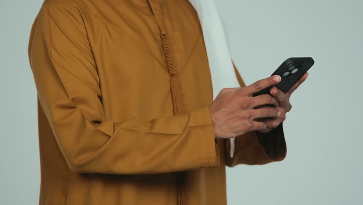 متابعه آخر أخبار السوشال ميديا، تصفح الانترنت وإنجاز المهام عن بعد، عقد اجتماع عمل، دمج التقنية والتكنولوجيا في الحياة اليومية, تصوير مقرب لرجل عربي خليجي اماراتي يرتدي الكندورة والغترة يقوم باستخدام جهاز التابلت, خلفية بيضاء