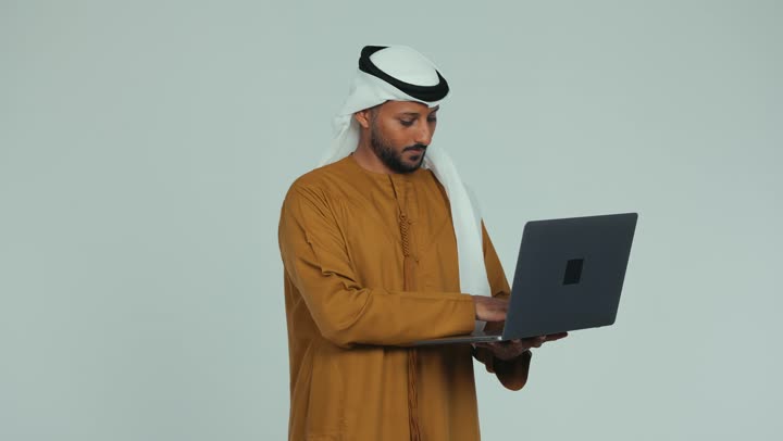 دمج التكنولوجيا في الحياة العملية، إدارة شؤون الأعمال وتنظيمها، استخدام التقنيات الحديثة المتطورة، عقد إجتماع عمل عبر الإنترنت، رجل عربي خليجي سعودي يرتدي الكندورة والغترة يقوم بالعمل على الحاسب المحمول,  خلفية بيضاء