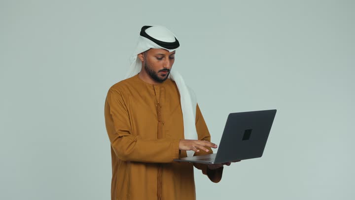 إلقاء التحية والسلام، ادارة وانجاز المهام باستخدام جهاز تقني حديث, تصوير مقرب لرجل عربي خليجي إماراتي يرتدي الكندورة والغترة البيضاء يقوم بإجراء اجتماع عمل عبر الحاسوب المحمول، مهن ووظائف مكتبية إماراتية، إجراء مكالمة فيديو مع الأهل والأصحاب، خلفية بيضاء
