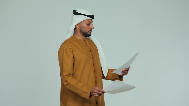 التدقيق في الملاحظات المكتوبة، اعداد التقارير الخاصة بالعمل، تصوير من الجانب لرجل عربي خليجي اماراتي يرتدي الكندورة والغترة يحمل بيده أوراق بيضاء، مراجعة ومتابعة الخطط والمشاريع، تبادل الخبرات والمهارات، خلفية بيضاء