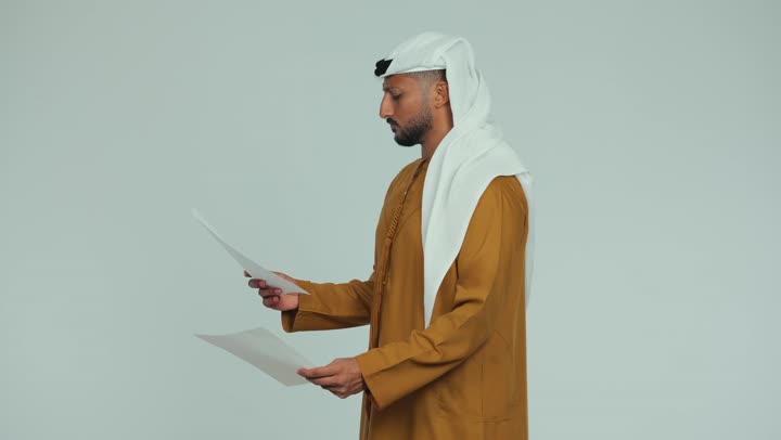 التدقيق في الملاحظات المكتوبة، اعداد التقارير الخاصة بالعمل، تصوير من الجانب لرجل عربي خليجي اماراتي يرتدي الكندورة والغترة يحمل بيده أوراق بيضاء، مراجعة ومتابعة الخطط والمشاريع، تبادل الخبرات والمهارات، خلفية بيضاء