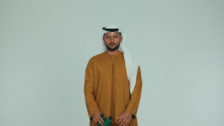 مراقبة ومشاهدة الأشياء البعيدة، الرؤية المستقبلية وتحديد الأهداف والطموحات، رجل عربي خليجي اماراتي يرتدي الكندورة والغترة يمسك بيده  منظار ثنائي العينين وينظر من خلاله بإيماءات السرور والسعادة، خلفية بيضاء