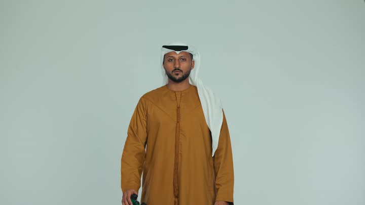 الإشارة بإصبع السبابة إلى شيء ما، مراقبة ومشاهدة الأشياء البعيدة، الرؤية المستقبلية وتحديد الأهداف والطموحات، رجل عربي خليجي اماراتي يرتدي الكندورة والغترة يمسك بيده  منظار ثنائي العينين وينظر من خلاله بإيماءات الذهول، خلفية بيضاء