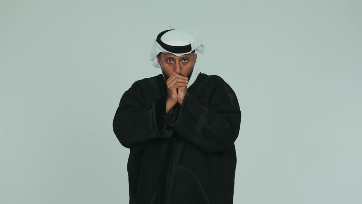 الأجواء الشتوية الباردة، الشعور بالصقيع والقشعريرة والتجمد، إيماءات وجه ويدين تدل على البرد الشديد، رجل عربي خليجي اماراتي يرتدي الفروة و والغترة يقوم بتغطية انفه وتدفئة يديه، ارتداء الملابس الدافئة في فصل الشتاء، خلفية بيضاء