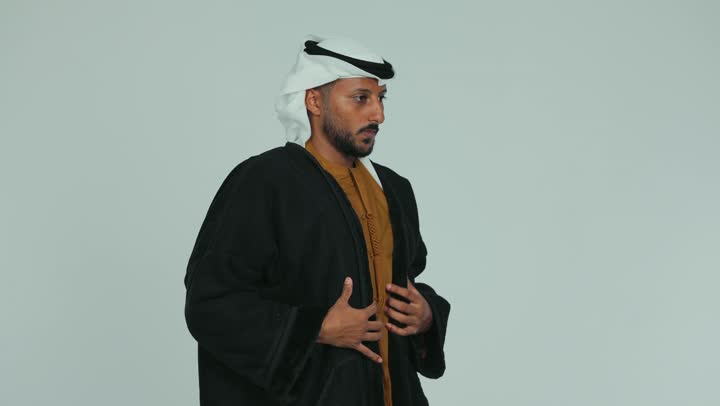 ارتداء الملابس الدافئة في فصل الشتاء، الأجواء الشتوية الباردة، الشعور بالصقيع والقشعريرة والتجمد، إيماءات وجه ويدين تدل على البرد الشديد، رجل عربي خليجي اماراتي يرتدي الفروة و والغترة يقوم تدفئة يديه، خلفية بيضاء