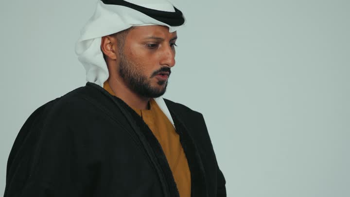 Feeling frostbitten, chills and freezing, wearing warm clothes in winter, cold winter weather, facial and hand gestures indicating extreme cold, close-up of an Emirati Gulf Arab man wearing a fur and ghutra warming his hands and covering his nose, white background