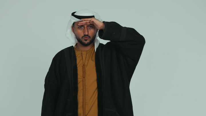 Wearing appropriate winter clothes, trying to see distant objects, feeling and sensing extreme cold, an Emirati Gulf Arab man wearing a fur and ghutra raising his hand with gestures of headache and head ache, white background