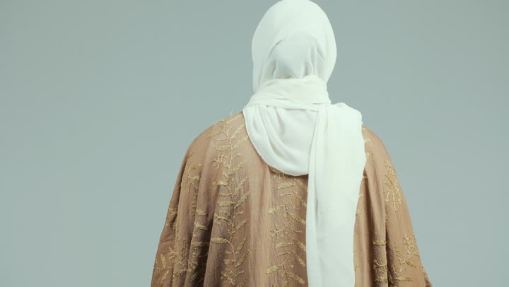 The concept of modesty and decency, elegance and interest in outward appearance and dress, a close-up shot from the back of a veiled Emirati Gulf Arab woman wearing an abaya, walking upright and confidently, the concept of femininity and kindness, white background