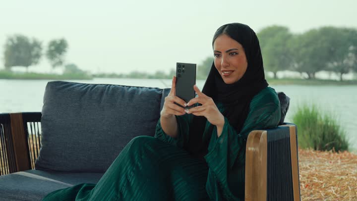 استخدام التكنولوجيا الحديثه ، سيده سعودية تقوم باستخدام الجوال ،قضاء وقت ممتع فى الخارج ، ايماءات السعاده والسرور، تصوير لامراة عربية خليجية اماراتية محجبة ترتدي العباءة تجلس على الأريكة في إحدى المقاهي الراقية تستمع بلحظات الهدوء والراحة