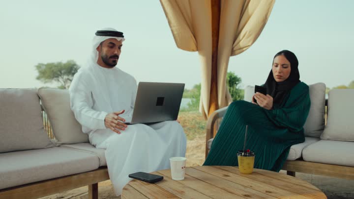رجل عربي خليجي اماراتي في اجتماع عمل ، تطوير الاعمال والاستراتيجيات, النجاح وتحقيق الاهداف، استخدم جهاز الحاسوب المحمول ، تصوير مقرب لرجل عربي خليجي اماراتي يجلس مع امرأه في المقهى ، انجاز المشاريع والمهام في الكافيه.