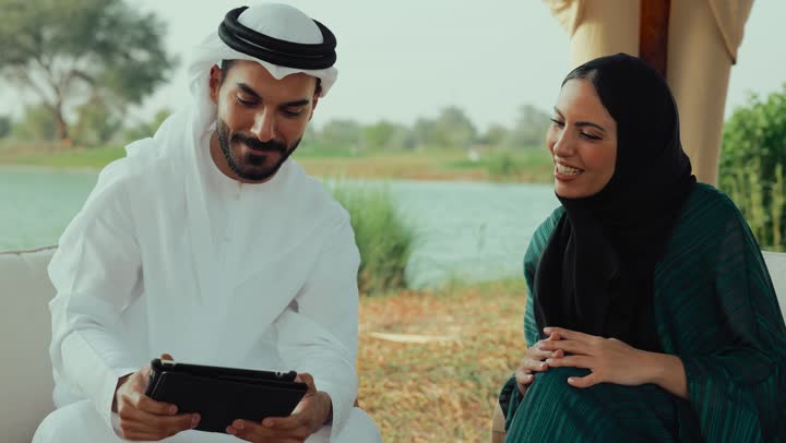 اجراء بث مباشر ، استخدام التقنيات الحديثة ،تعابير السعادة والسرور بلمة الرفاق، التسامر والدردشة وقضاء وقت ممتع مع الأصدقاء، كوفي شوب راقي بالامارات، تصوير مقرب لرجل عربي خليجي اماراتي وامرأته يجلسون في المقهى ، اجراء مكالمات الفيديو .