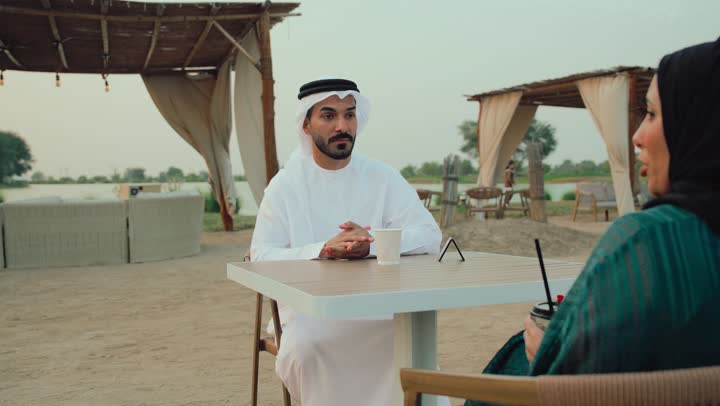 ايماءات الترحيب بالضيف ، تصوير مقرب لرجل عربي خليجي اماراتي وامرأته يجلسون في المقهى يستمتعون بالنقاش معاً ، ايماءات السرور والسعادة، حوار ونقاش اسري، انشطة وفعاليات ترفيهية عائلية، مفهوم الألفة والمحبة بين أفراد الأسرة، التسلية والترفيه بالعطلات .