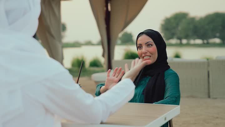 Family entertainment activities and events, the concept of intimacy and love between family members, entertainment and recreation during holidays, family dialogue and discussion, gestures of pleasure and happiness, a close-up of an Arab Gulf Emirati man and his wife sitting in a cafe enjoying a discussion together.