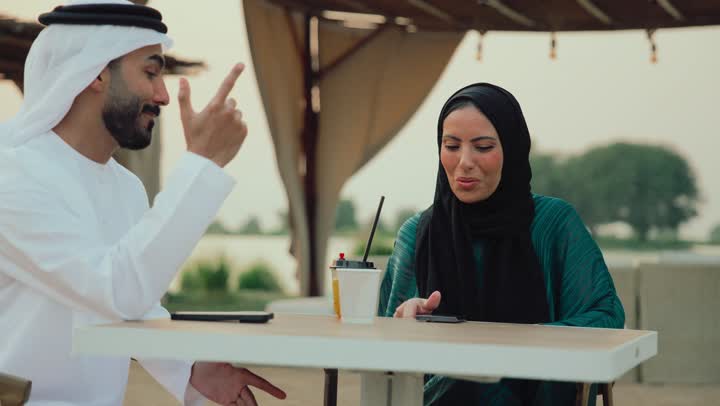 التسامر والدردشة وقضاء وقت ممتع مع الأصدقاء، تعابير السعادة والسرور بلمة الرفاق، استخدام التقنيات الحديثة ، كوفي شوب راقي بالامارات،  تصوير مقرب لرجل عربي خليجي اماراتي وامرأته يجلسون في المقهى ،يلتقطون السيلفي عبر الجوال لتوثيق الذكريات .