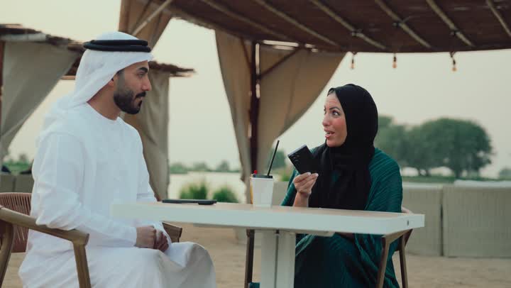 استخدام التقنيات الحديثة ،تعابير السعادة والسرور بلمة الرفاق، التسامر والدردشة وقضاء وقت ممتع مع الأصدقاء، كوفي شوب راقي بالامارات،  تصوير مقرب لرجل عربي خليجي اماراتي وامرأته يجلسون في المقهى يلتقطون السيلفي لتوثيق الذكريات .